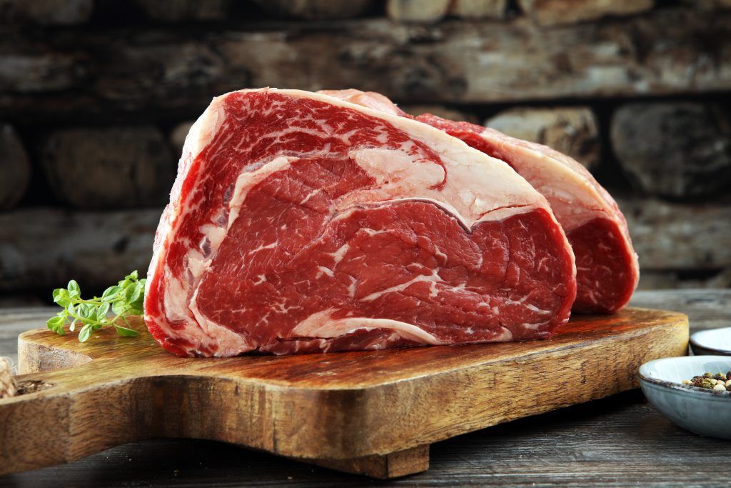 Raw fresh meat Ribeye Steak, seasoning and meat fork on dark background Raw fresh meat Ribeye Steak, seasoning and meat fork on dark background