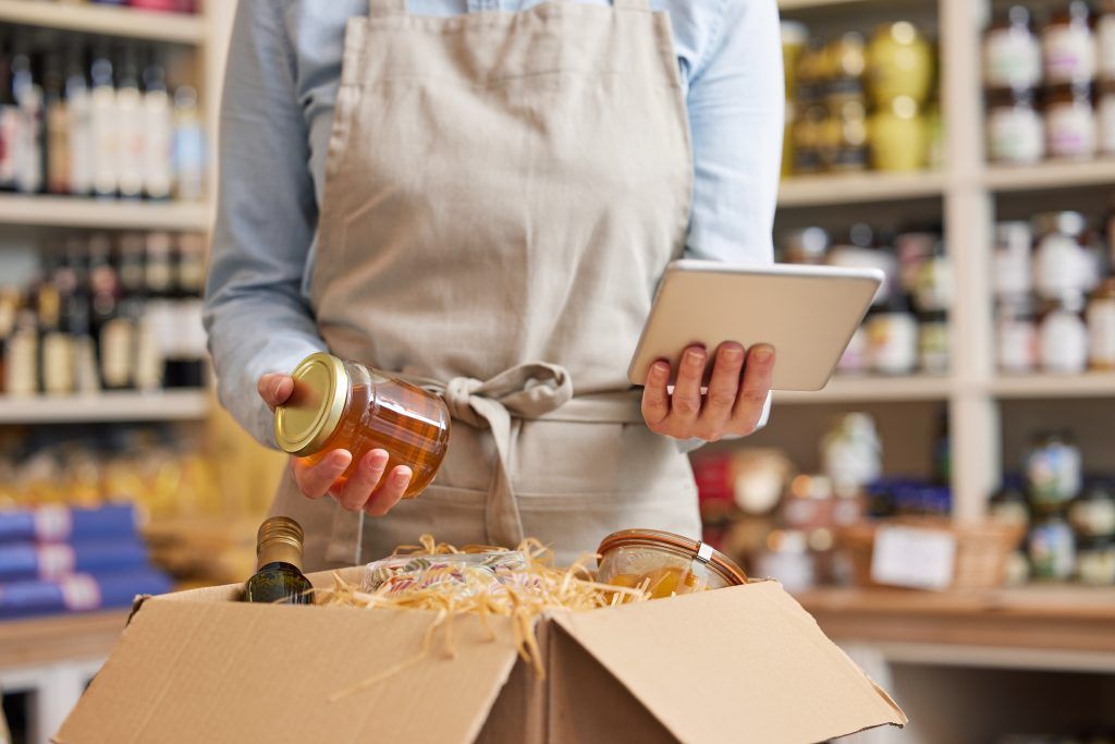 Close Up Of Female Owner Of Delicatessen Food Shop With Digital Tablet Preparing Online Grocery Order Close Up Of Female Owner Of Delicatessen Food Shop With Digital Tablet Preparing Online Grocery Order
